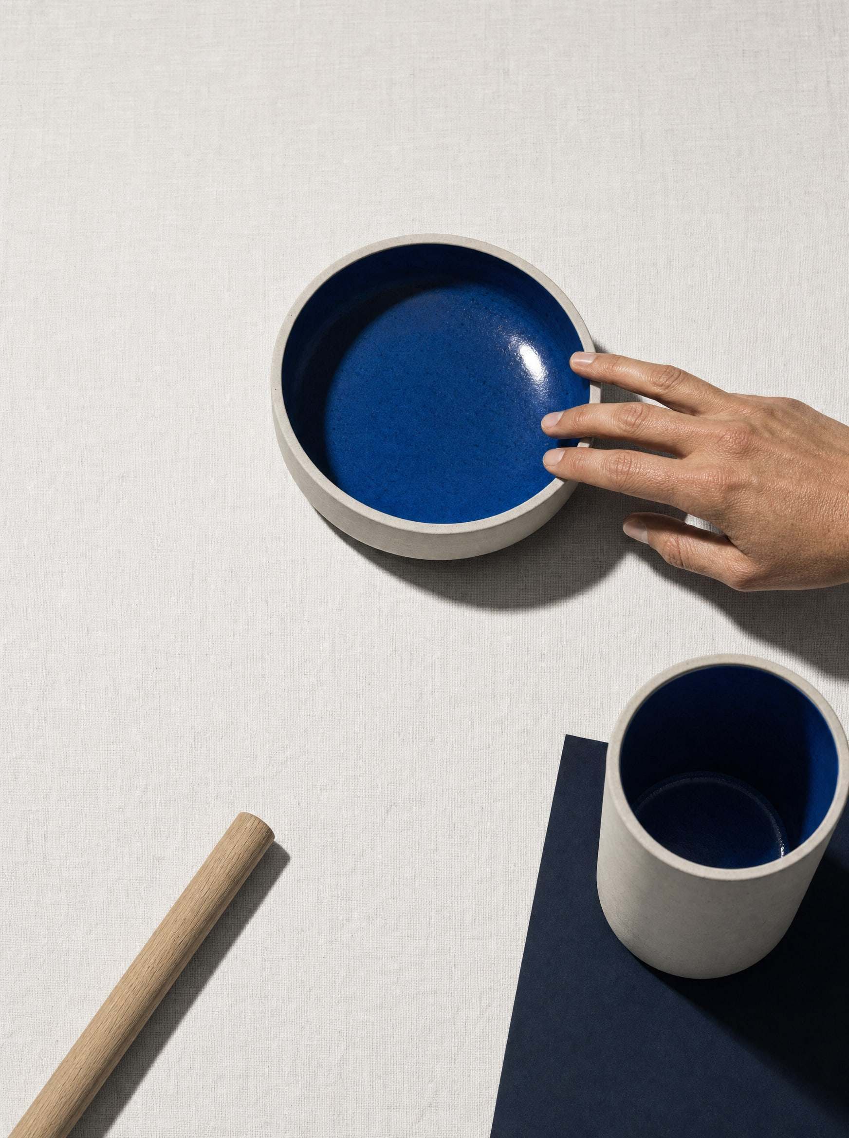 A hand arranging blue ceramic bowls on a bright table.